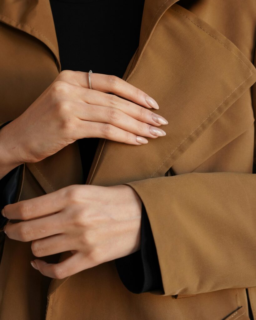 Close-up of woman's hands in a brown coat showcasing minimalist silver ring.